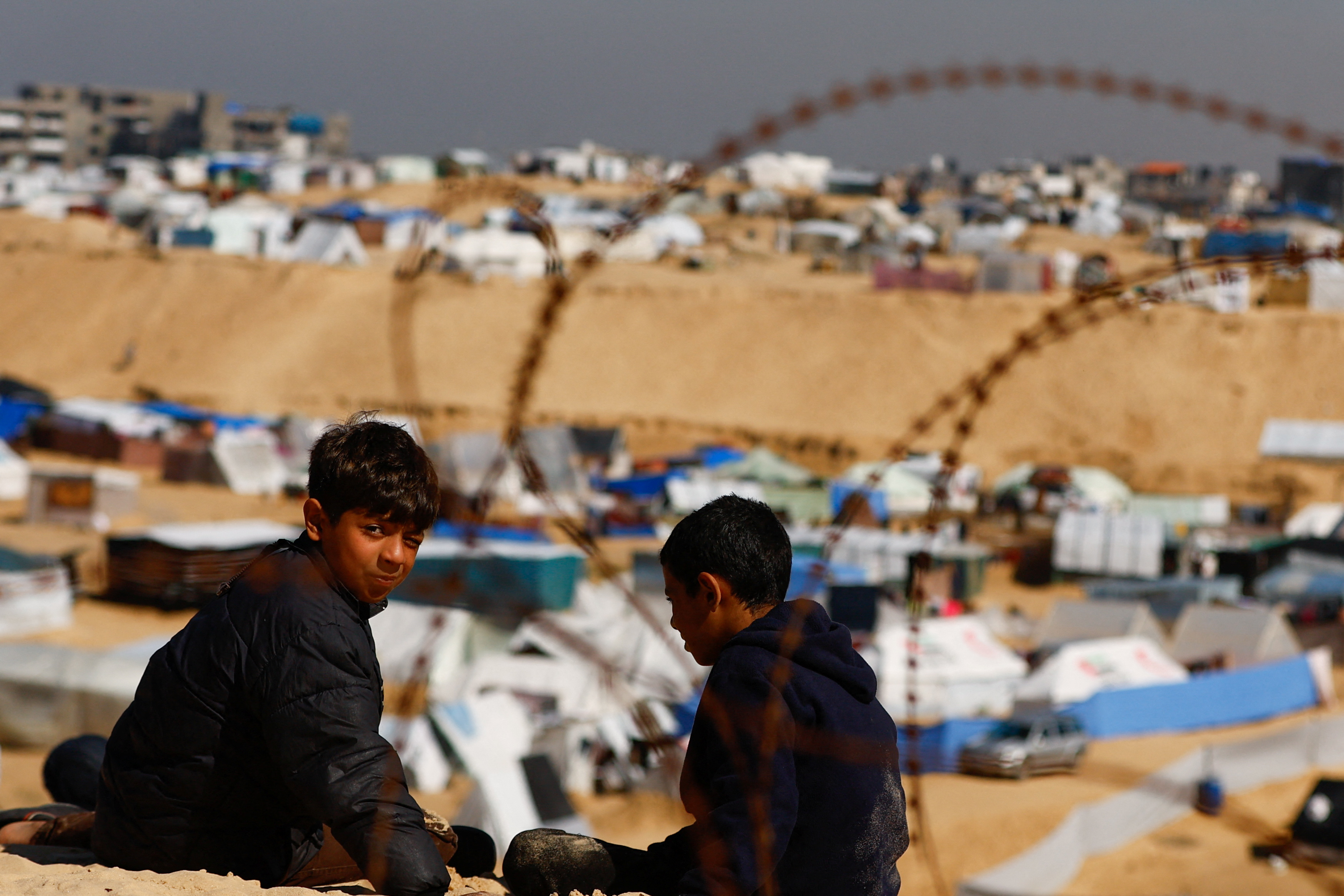 Boys sit outside, as displaced Palestinians, who fled their houses due to Israeli strikes, take shelter in a tent camp, amid the ongoing conflict between Israel and the Palestinian Islamist group Hamas, at the border with Egypt, in Rafah in the southern Gaza Strip, February 8, 2024. REUTERS/Ibraheem Abu Mustafa