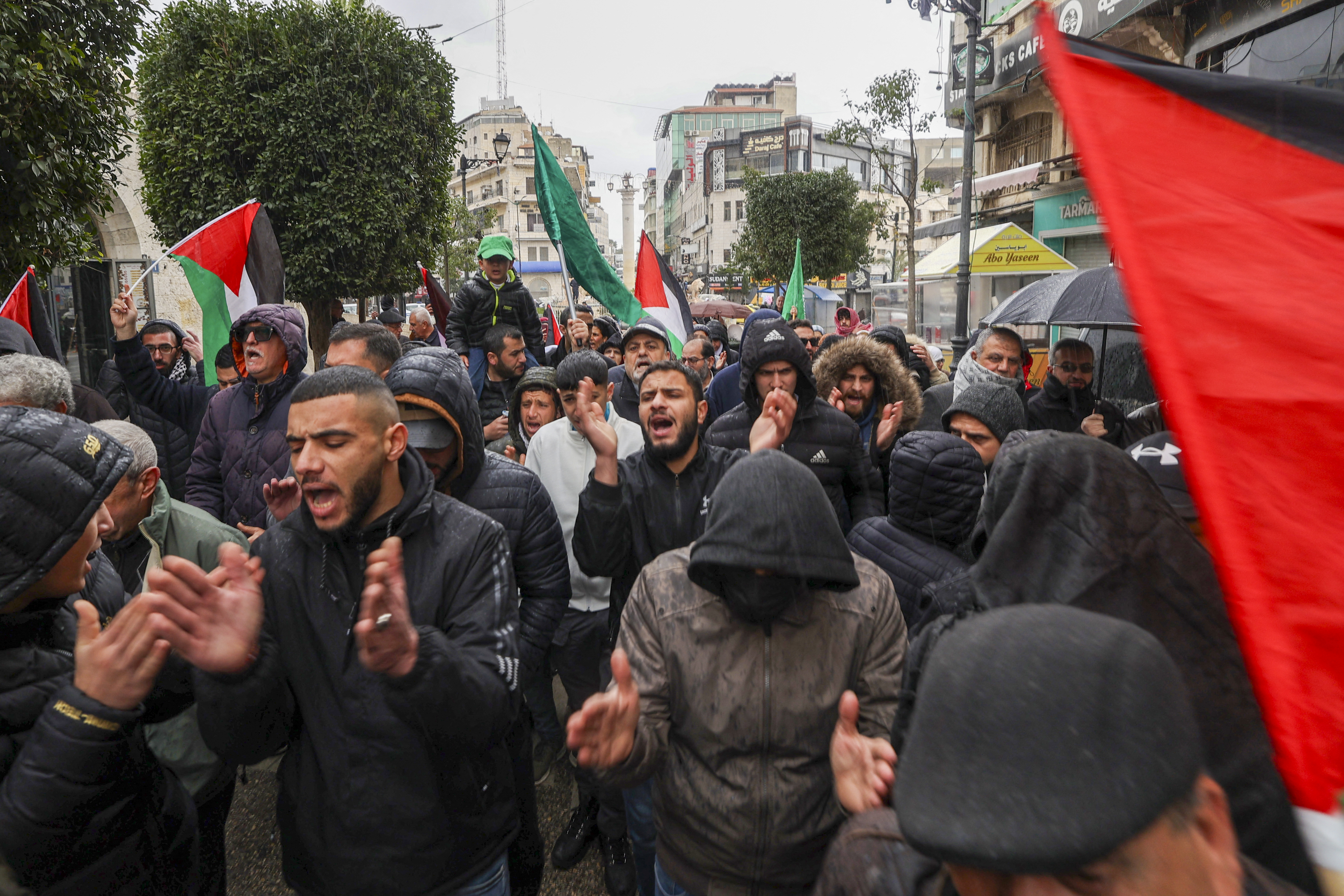 people wearing dark coloured clothes protest holding palestinian flags
