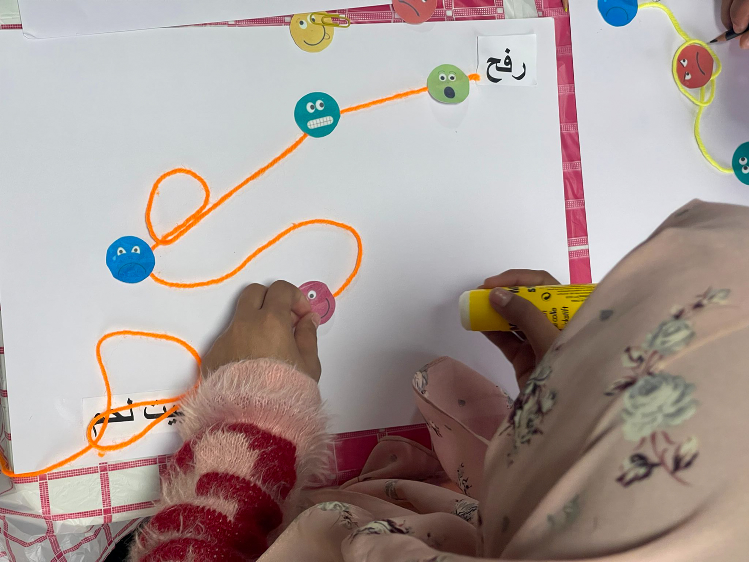 look over the shoulder of a little girl who's glueing her yarn and faces